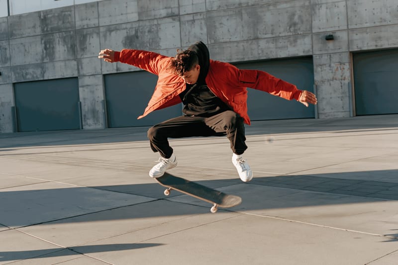 A skateboarder in a red jacket mid-trick in an empty concrete lot