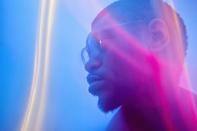 Profile of a man in glasses lit by streaks of blue and pink light